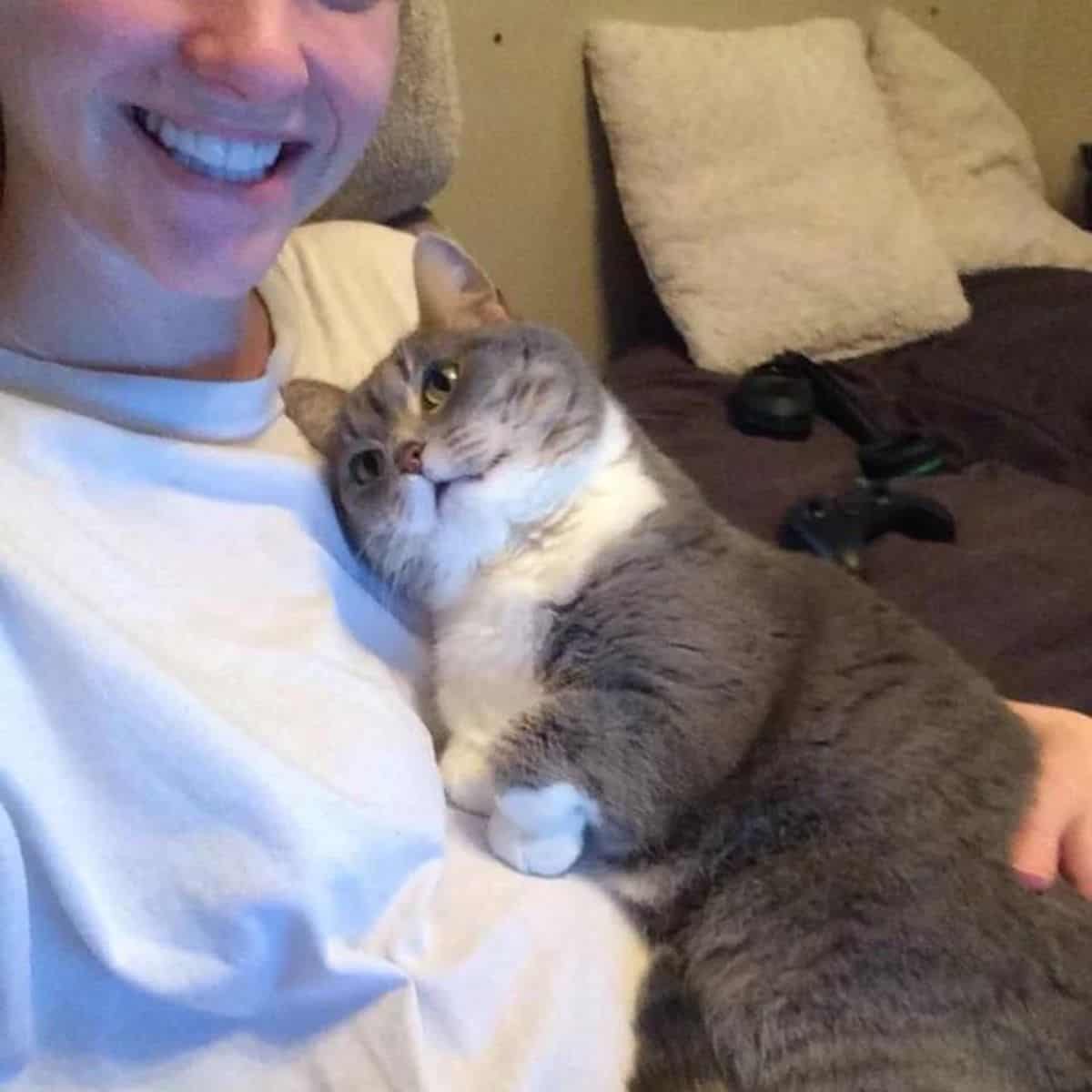 a smiling girl holds a cat on her chest