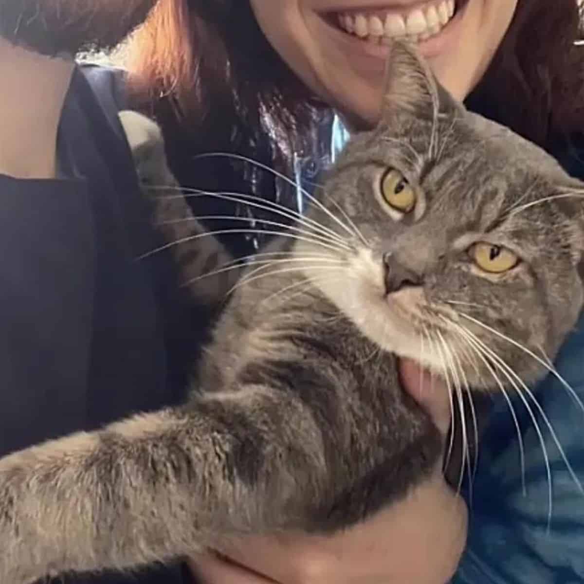 a smiling girl takes a picture with a cat in her arms