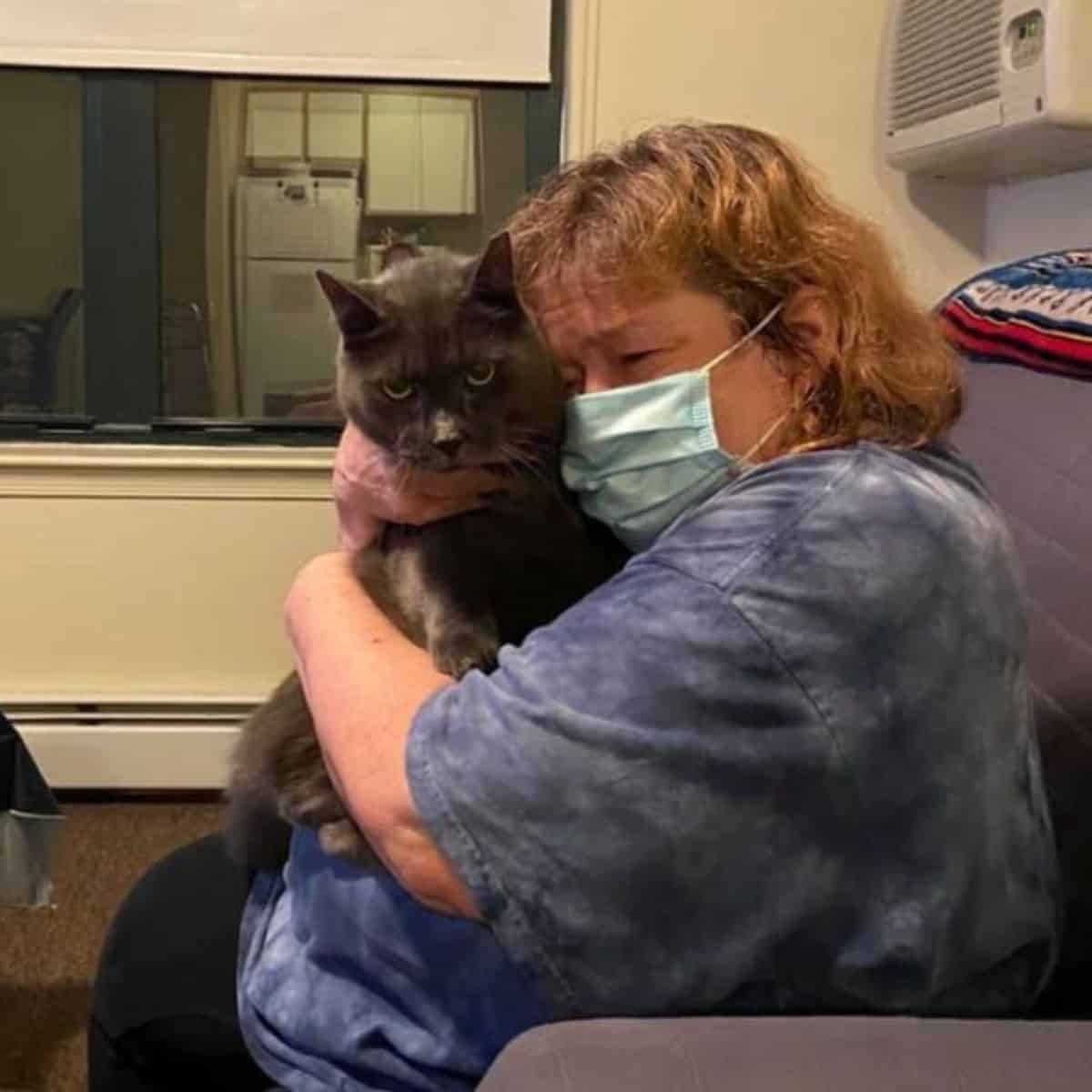 an elderly woman with a mask holds a cat in her arms