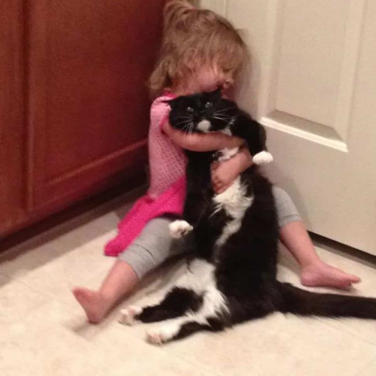 the little girl sits by the door and hugs the cat